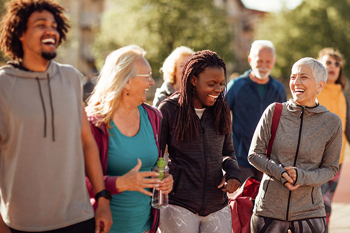 A group of adults of varying ages walks together outdoors while talking and laughing.