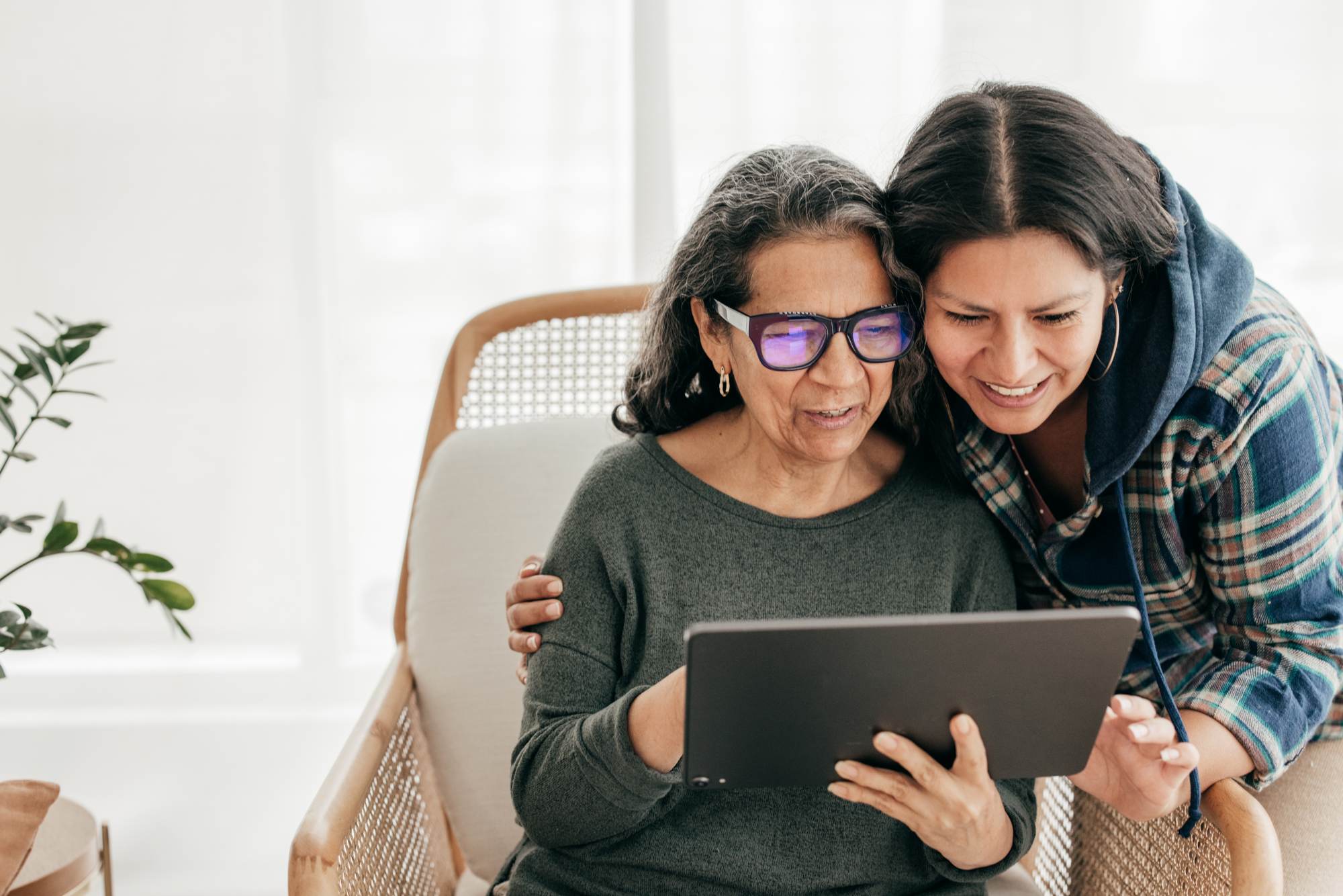 A woman helps her older mother use a tablet.