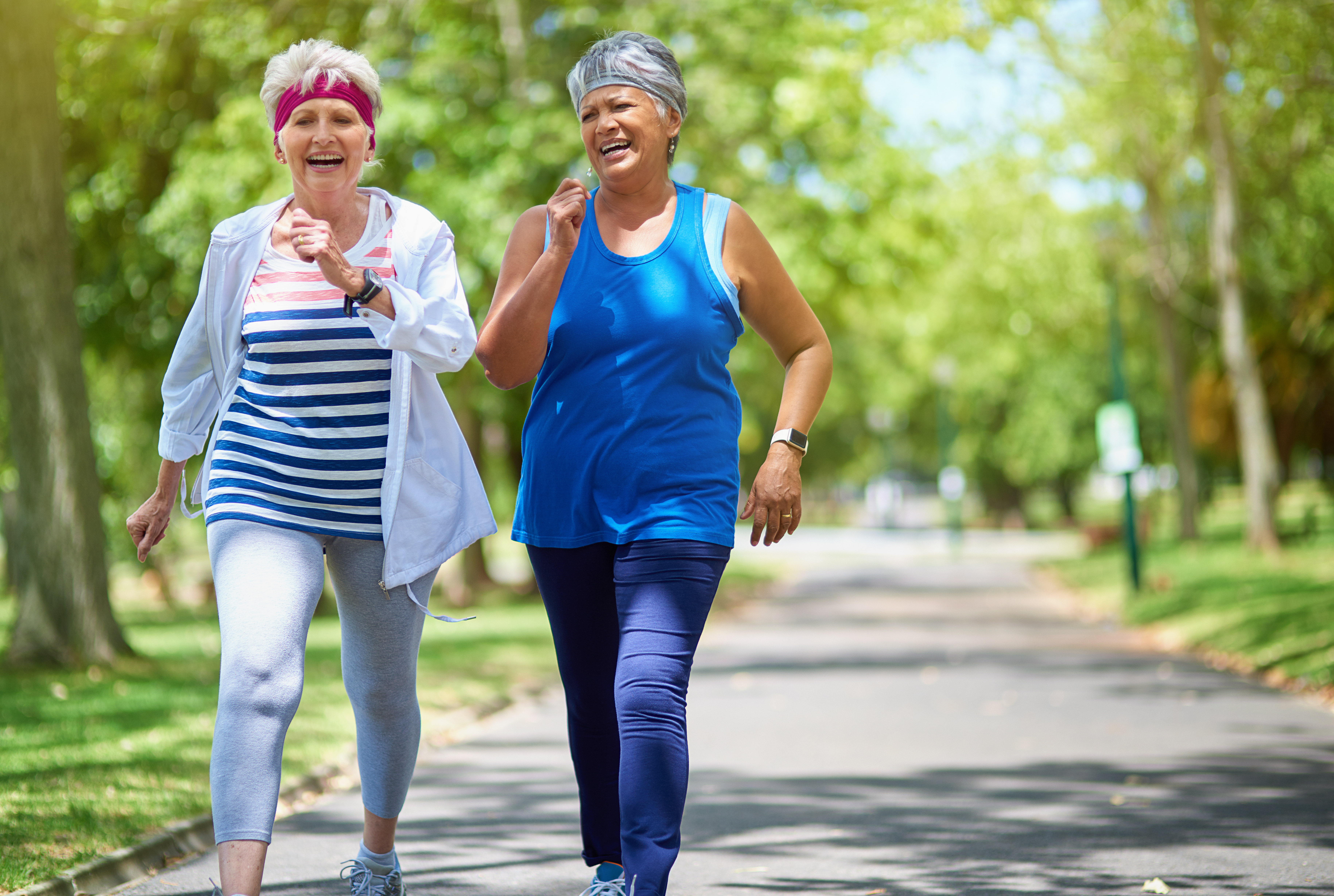 Two women in their 60's walking briskly in a park.