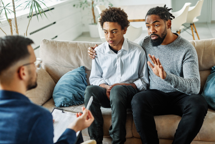 A father and son speak with a therapist.