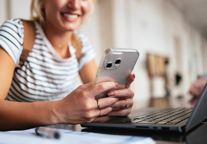 A girl, sitting at a laptop, is visible texting on her phone.