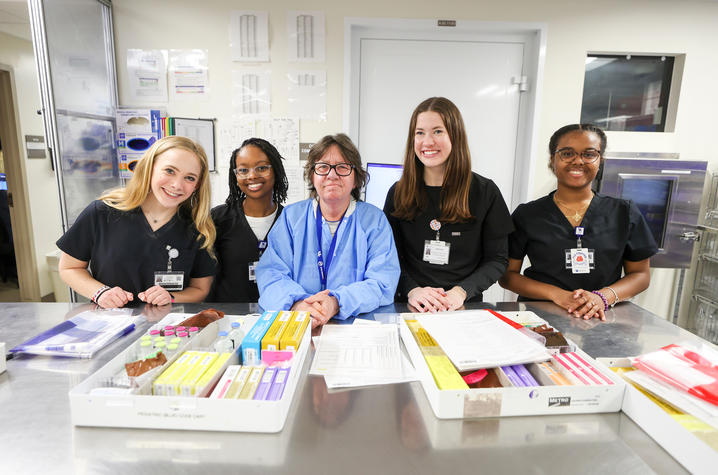 Four students and an instructor posing for a photo inside an educational pharmacy program.