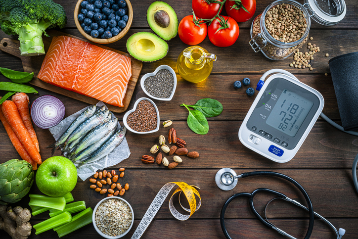 Heart-healthy foods like salmon and avocados are posed next to a blood pressure monitor.