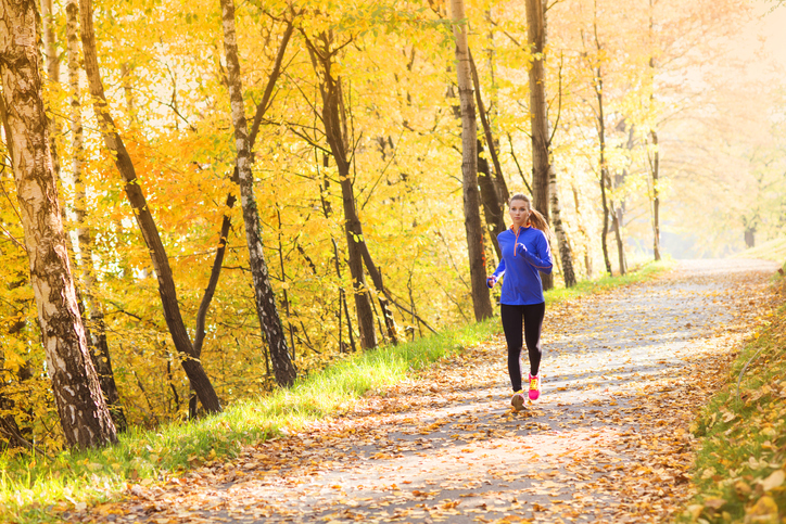 A woman runs through a trail in a hilly forest.