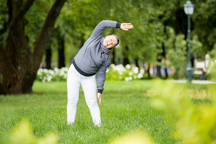 An older woman practicing yoga in a park.