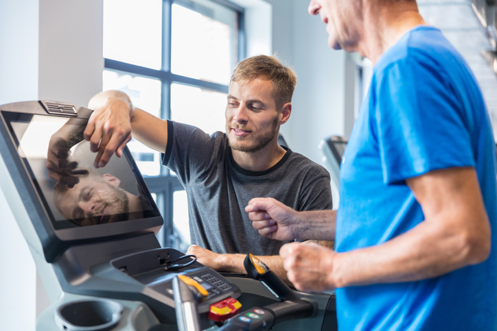 A rehab professional works with a patient on a cardio machine.