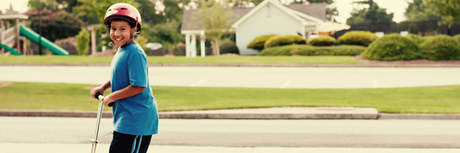 A boy wearing a helmet rides a scooter.