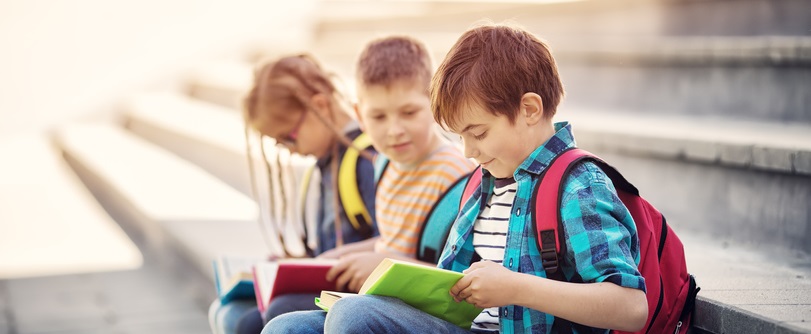 Three children sit on steps as they read.