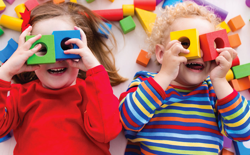 Two children playing with blocks peek through them.