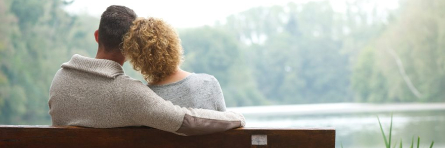 A couple seated on a bench overlooking a lake.