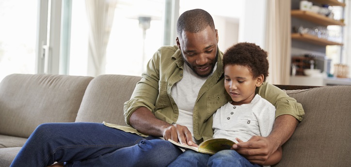 Dad and son read together on the couch.