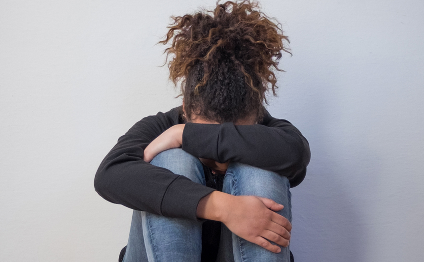 A depressed young woman pulls her knees to her chest and rests her head.