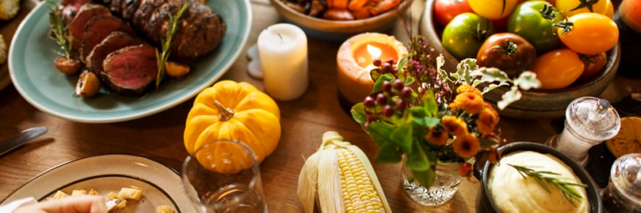 A fall table with roast beef, corn, squash and other vegetables.