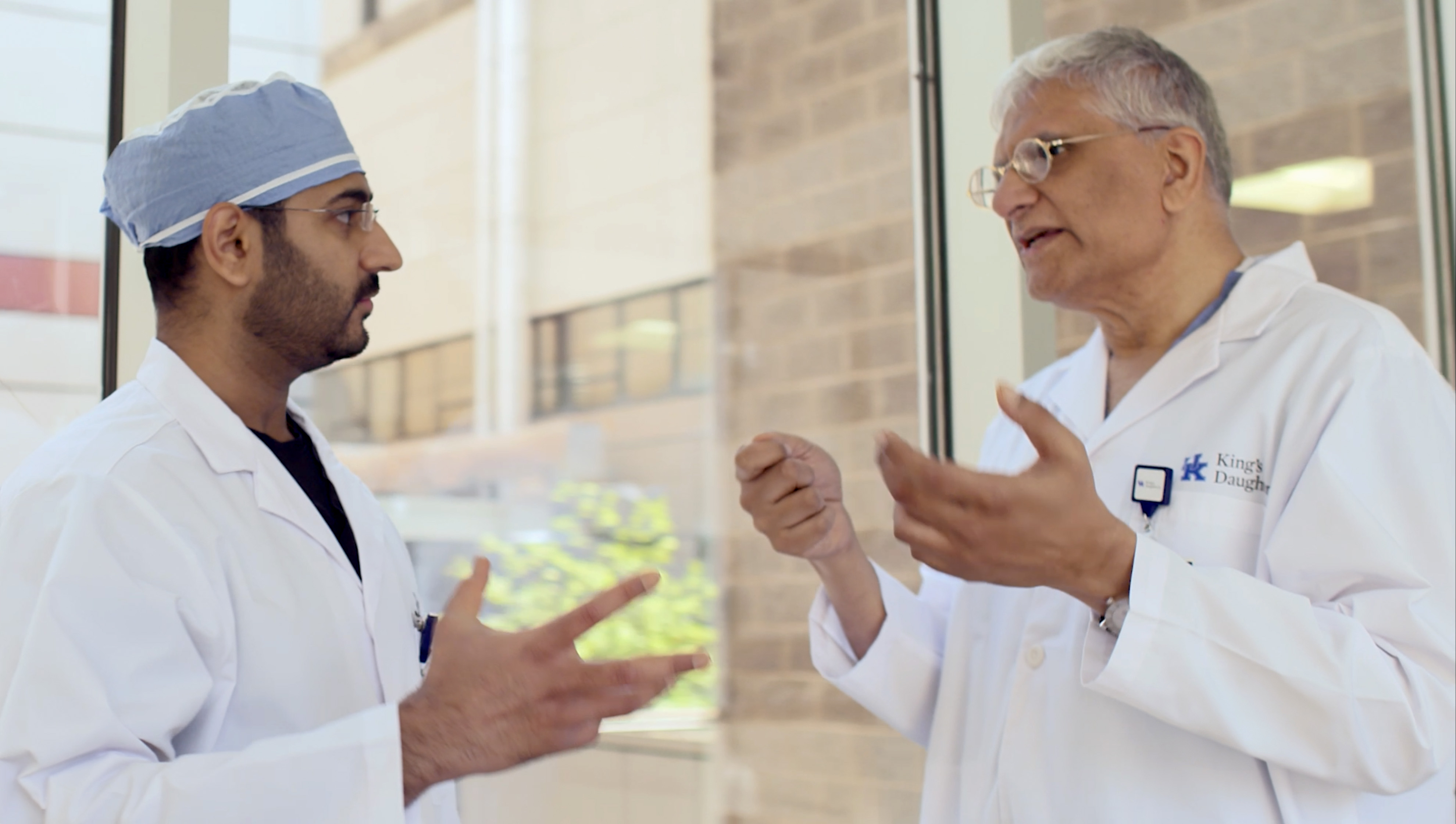 Two doctors speak to one another outside of a building.