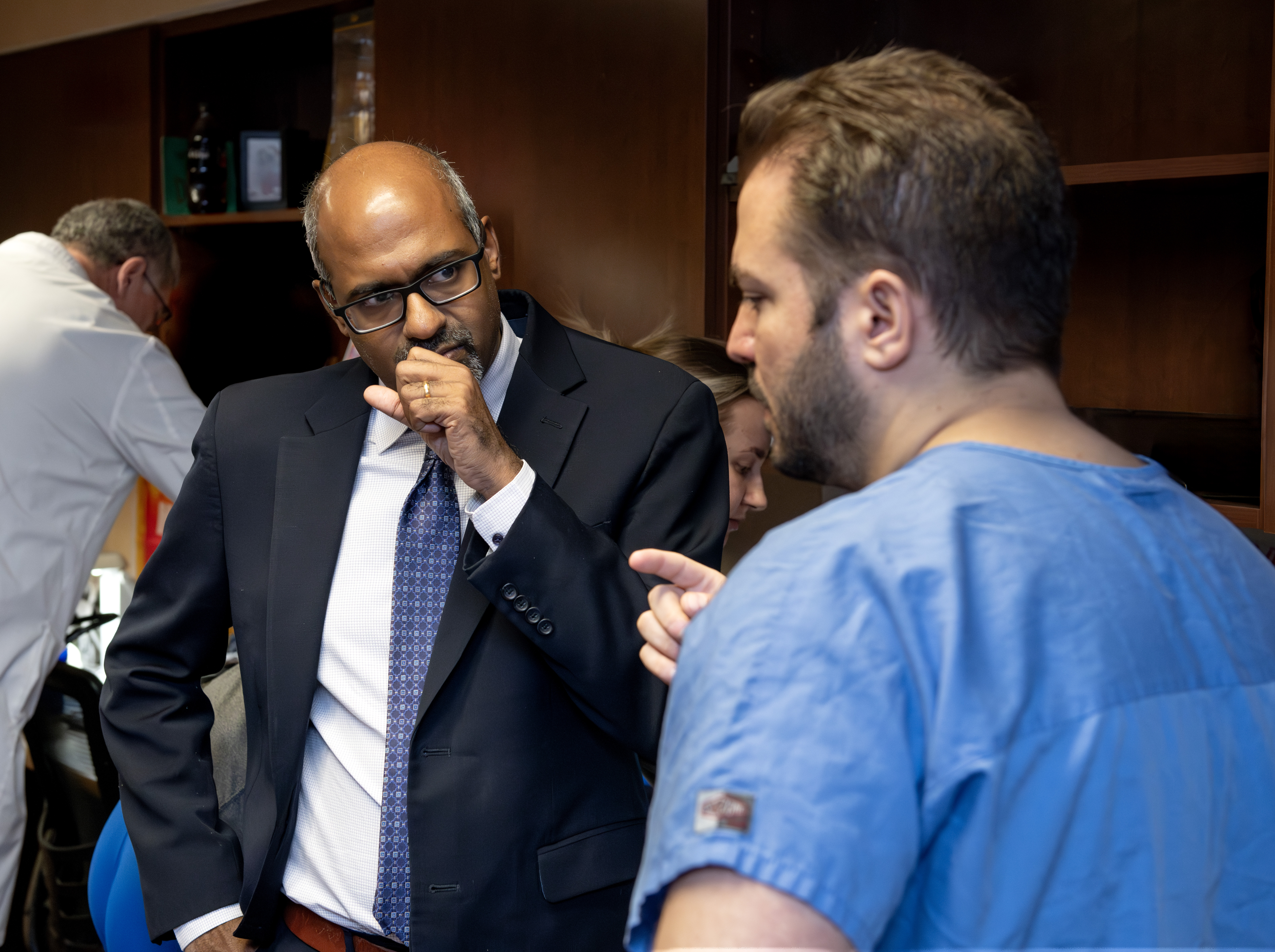 A man in a suit listens while a health care provider in scrubs speaks to him.