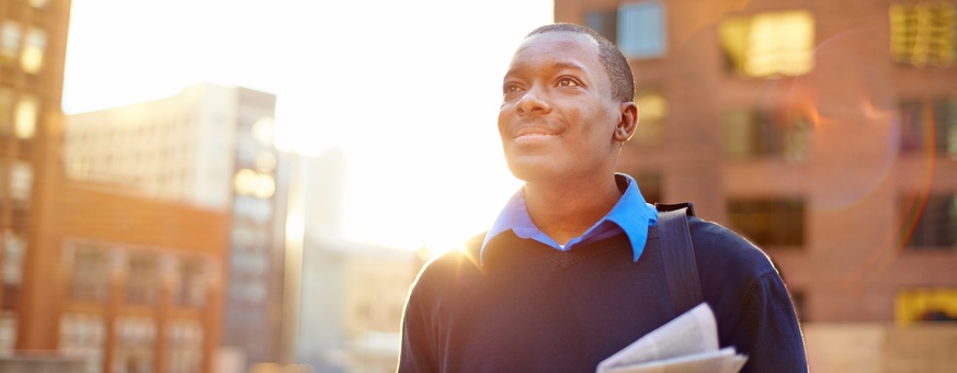 A man with a newspaper in his hand smiles and gazes at the city.