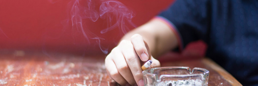 A man's hand shown holding a burning cigarette.