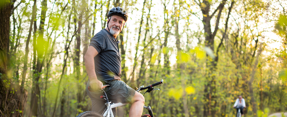 A man stops his bike in the forest and looks back.