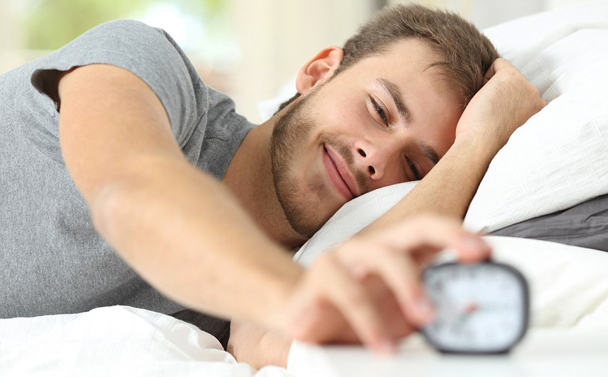 A man wakes up in bed and turns off his alarm clock.