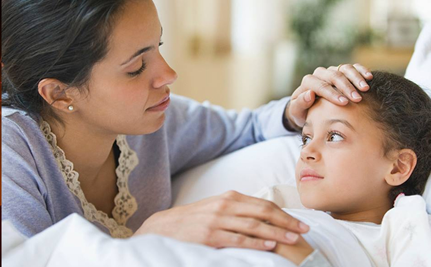 A mother checks her daughter's temperature by placing her hand on the child's forehead.