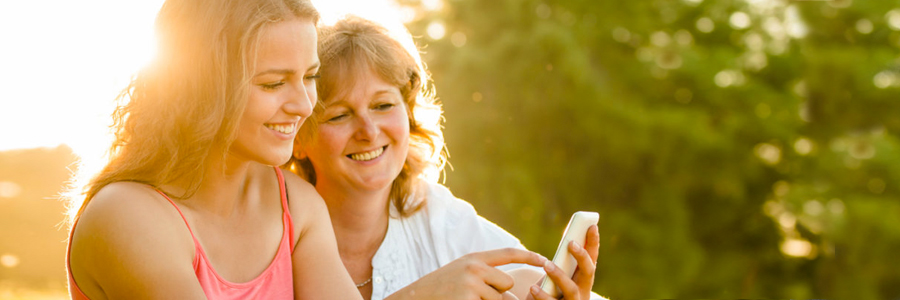 A mother looks on as her teen daughter uses a cellphone.