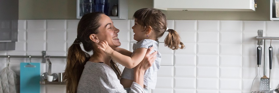 Mother picking up daughter in kitchen.