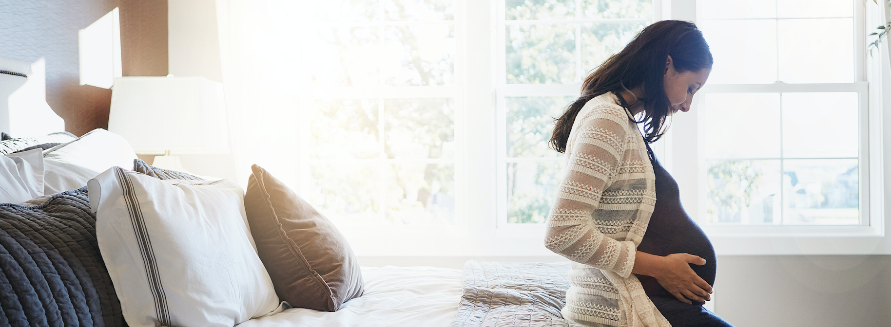 Pregnant woman sitting on bed. 