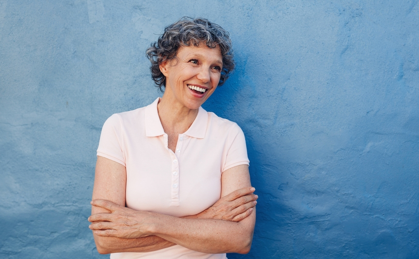 A smiling senior woman stands with her arms folded.