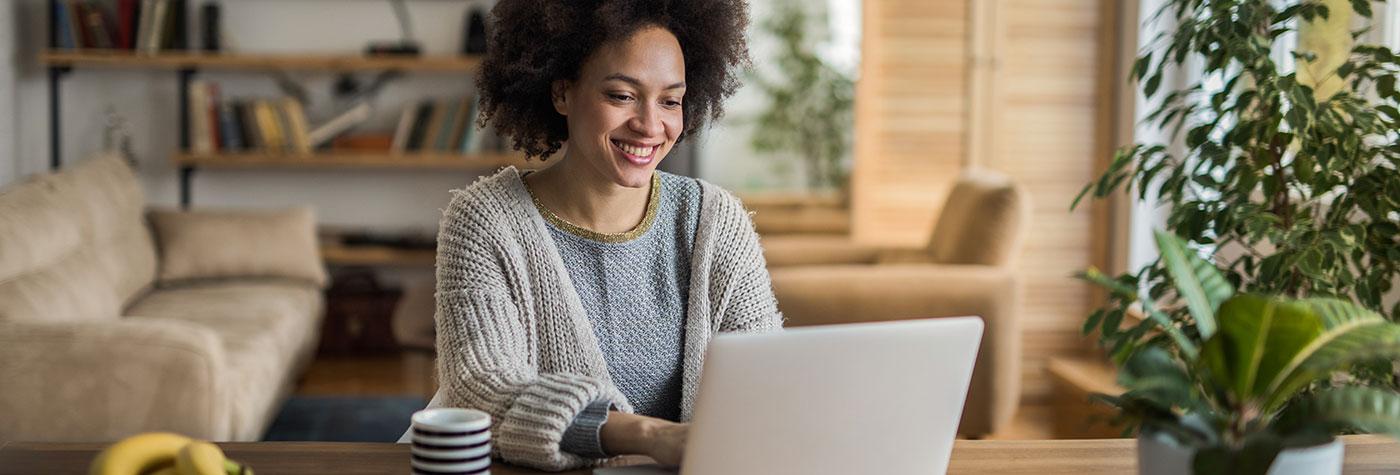 Smiling African-American types on a laptop computer while seated at her kitchen table