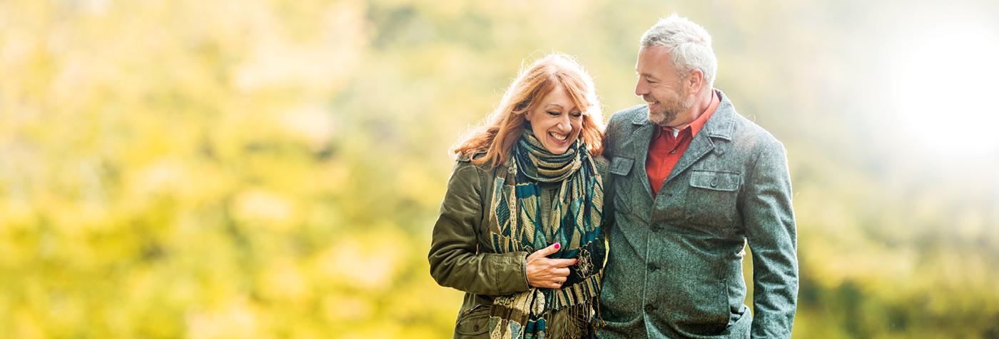 An older man and woman walk side by side through a park.