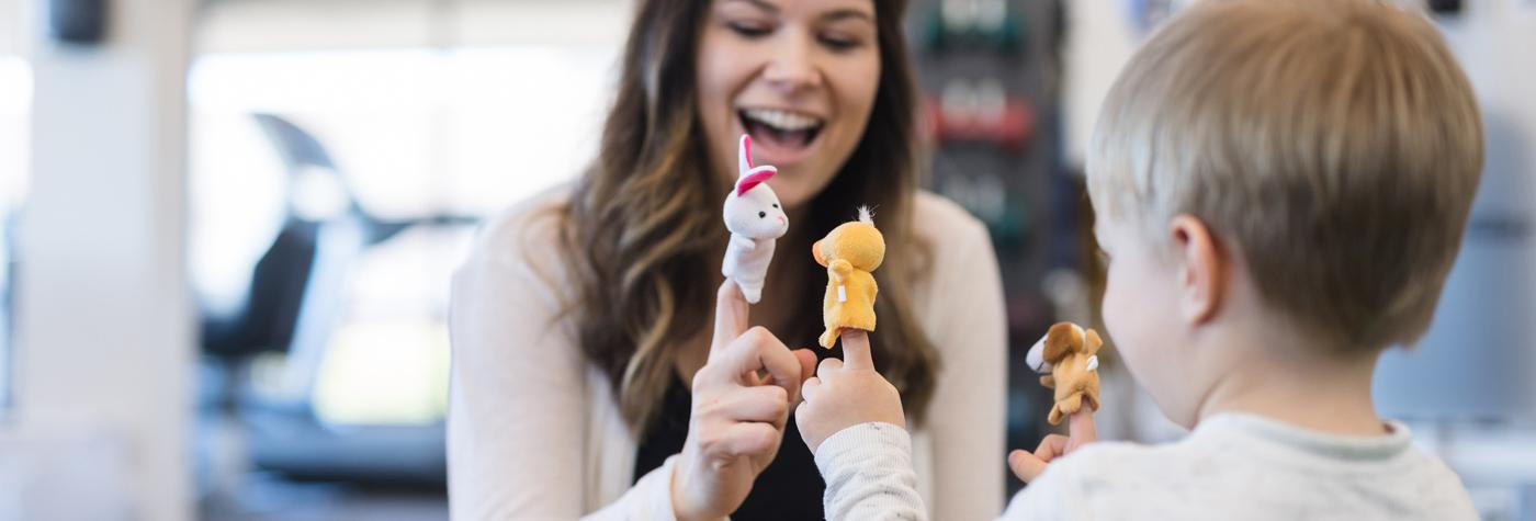 A female child life specialist and a young boy act out a story with finger puppets.