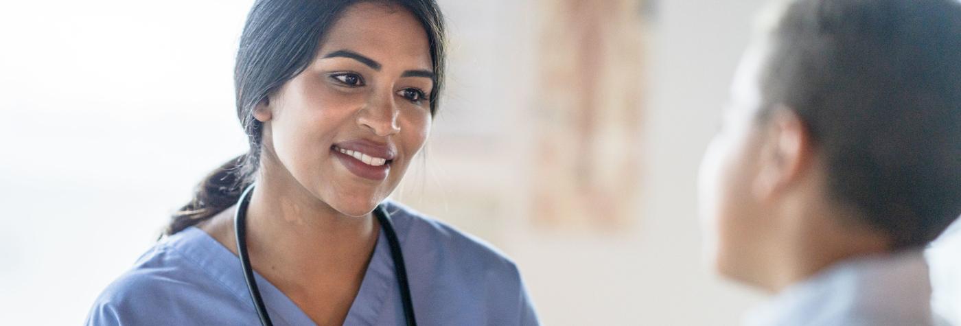 A female provider in a blue scrub top speaks with a patient. 