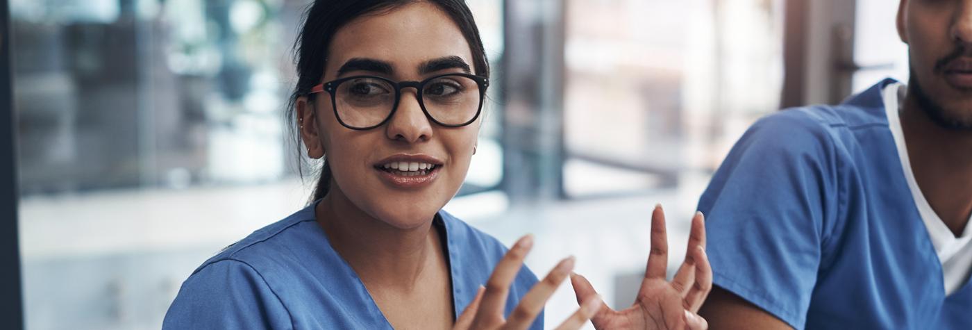 A female provider wearing a blue scrub top tells a story while sitting at a table with her colleagues.