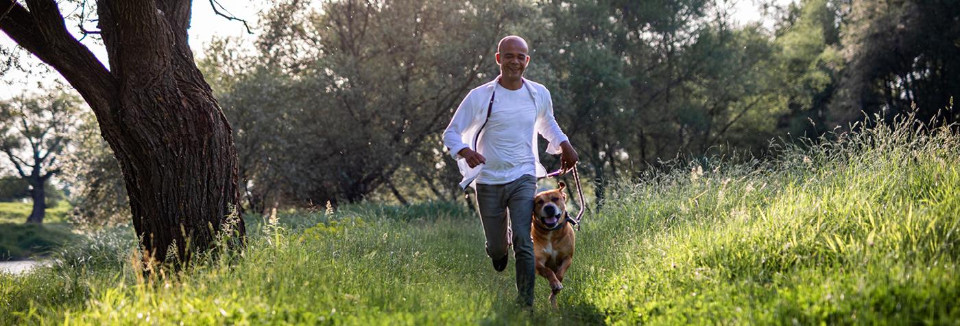 A man and his dog run through a greenspace in a park. 