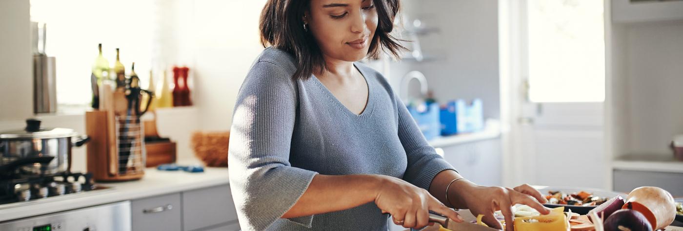 An African-American woman cuts up a variety of vegetables at the counter in her kitchen. 