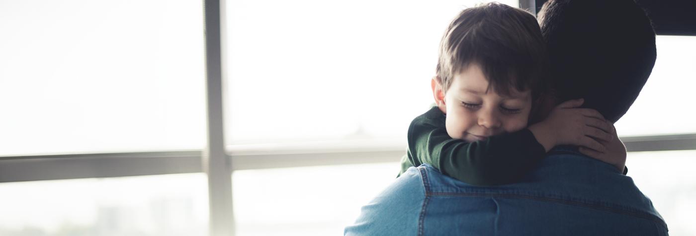 A young boy with closed eyes and a gentle smile embraces an adult male.