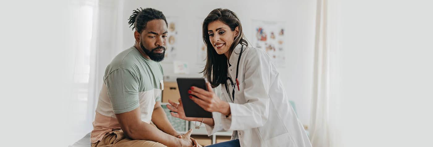 A female doctor in a white coat discusses information on a tablet computer with a young adult male patient 