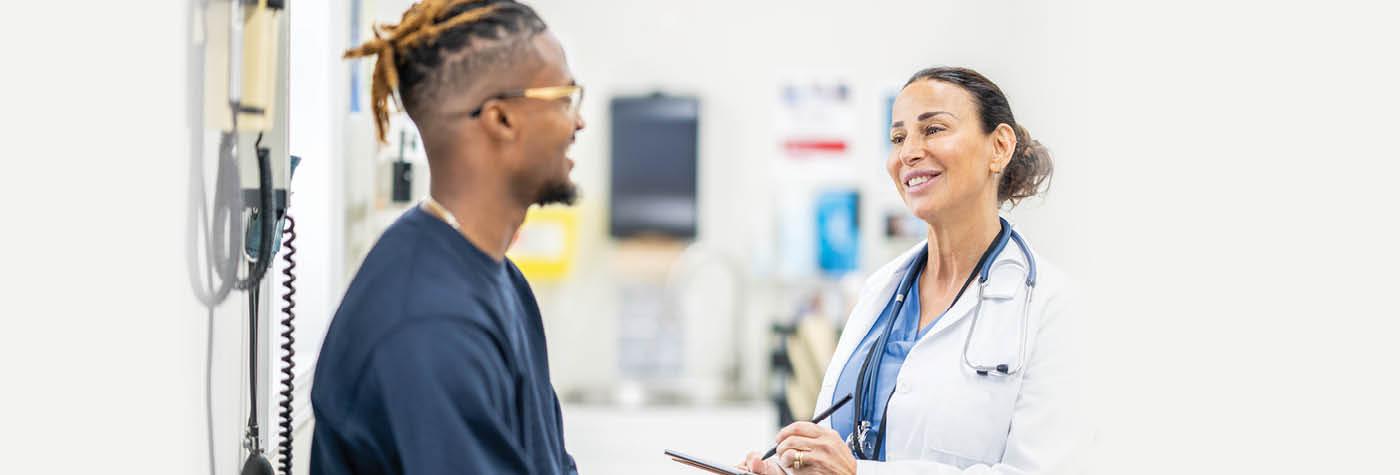 A young man smiles as he speaks with his doctor, a smiling woman wearing a white coat. 