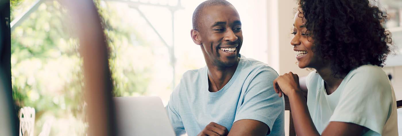 A young African-American man and woman sit side by side and laugh as they converse with one another.