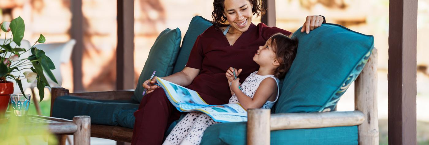 A mother and daughter sit side by side on a couch and look at a book together.