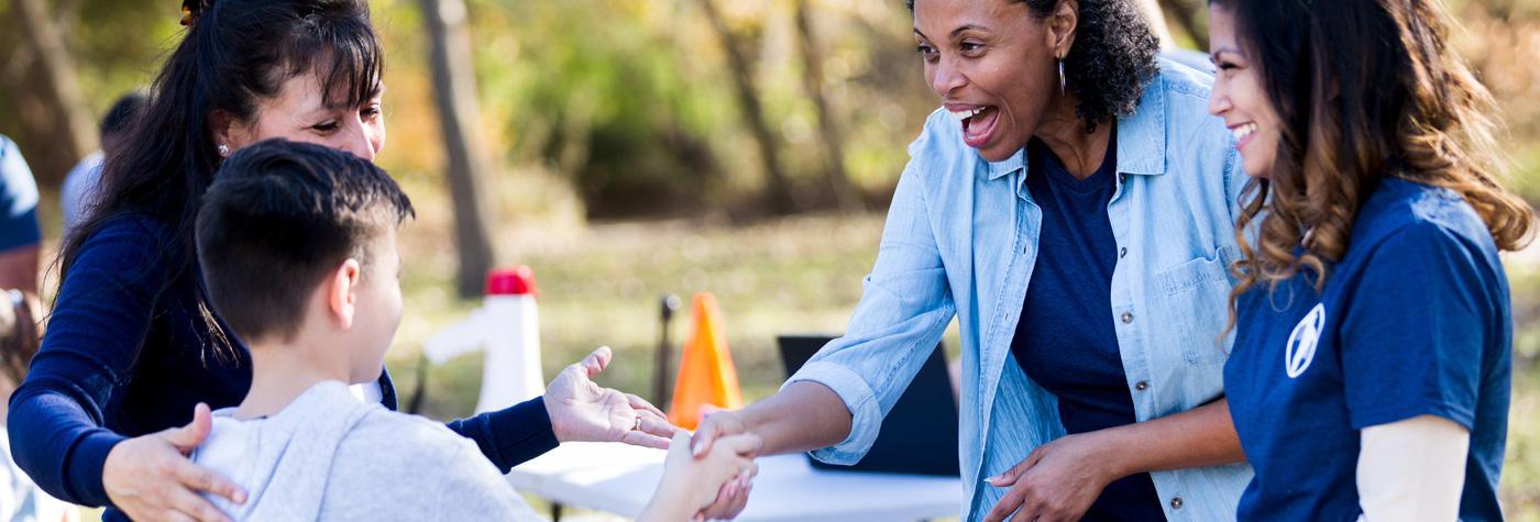 A young boy and his mother talk to healthcare workers at a table during an event taking place outdoors. 