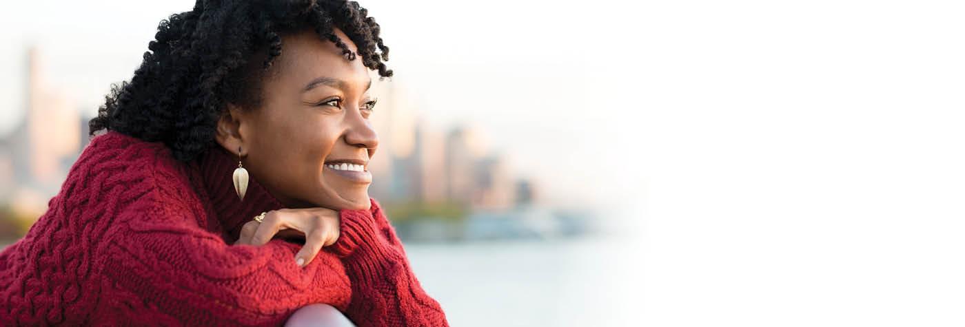 A young African American woman wearing a red sweater smiles as she looks into the distance.