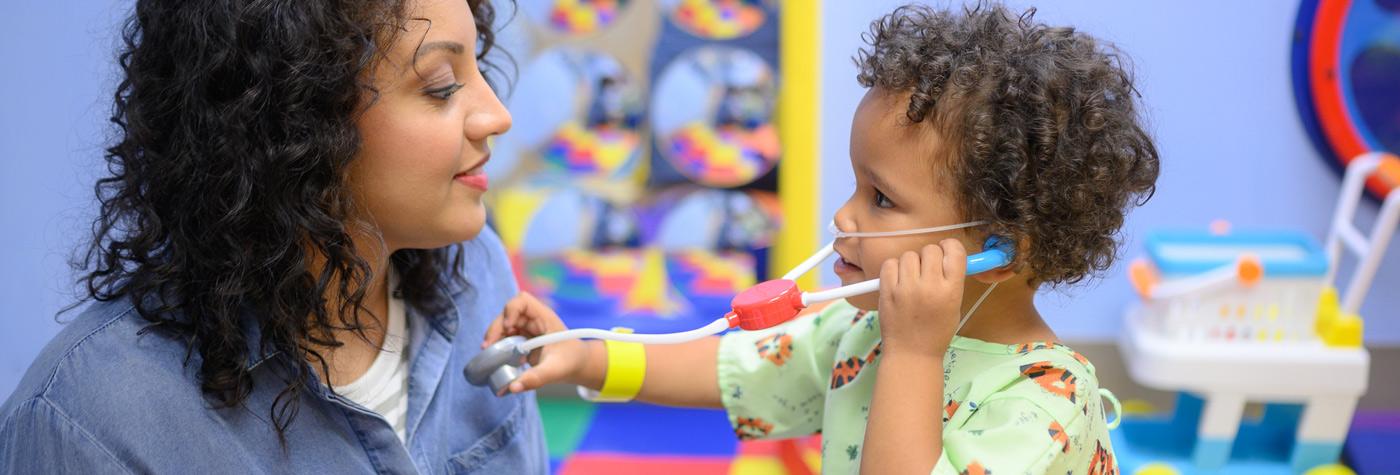 A mother and her young child playing with a toy stethoscope in doctor's office.