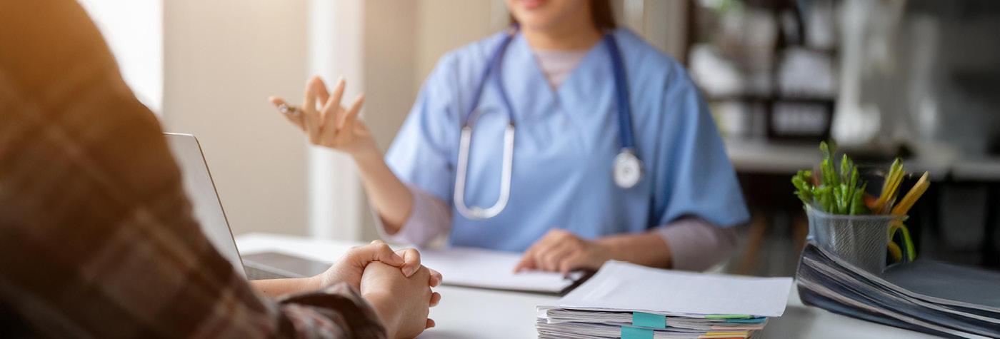 A doctor sits behind a desk and speaks with her patient.