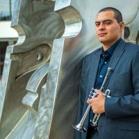 Adiel Nájera poses with his trumpet in front of an outdoor sculpture on the University of Kentucky campus.