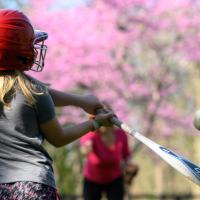 Sarah Beth, wearing a red batter's helmet, hits a softball thrown to her by her mother.