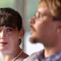 Sarah Custer, crying while focused in the background, looks toward her husband Dave, out of focus