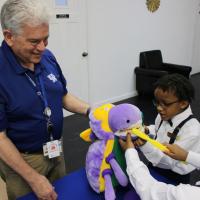 Two young boys learn how to brush a stuffed animal's teeth, assisted by an event volunteer.