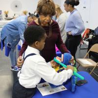 A young boy learns how to brush a stuffed animal's teeth, assisted by an event volunteer.