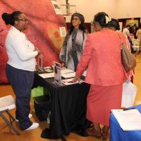 A group of women stands around a table and has a conversation.